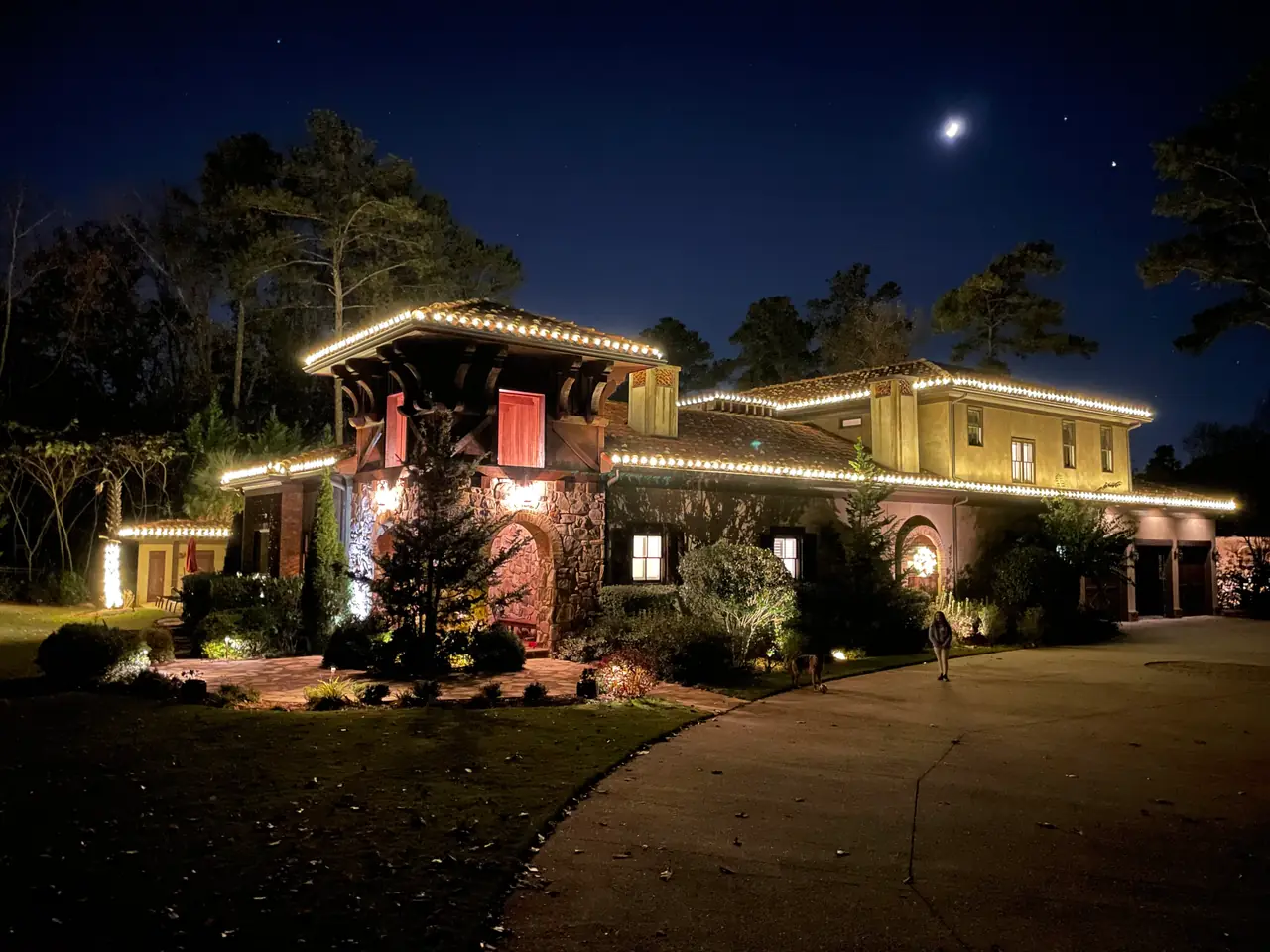 Warm white lights trace the rooflines and entrance of a home at night.