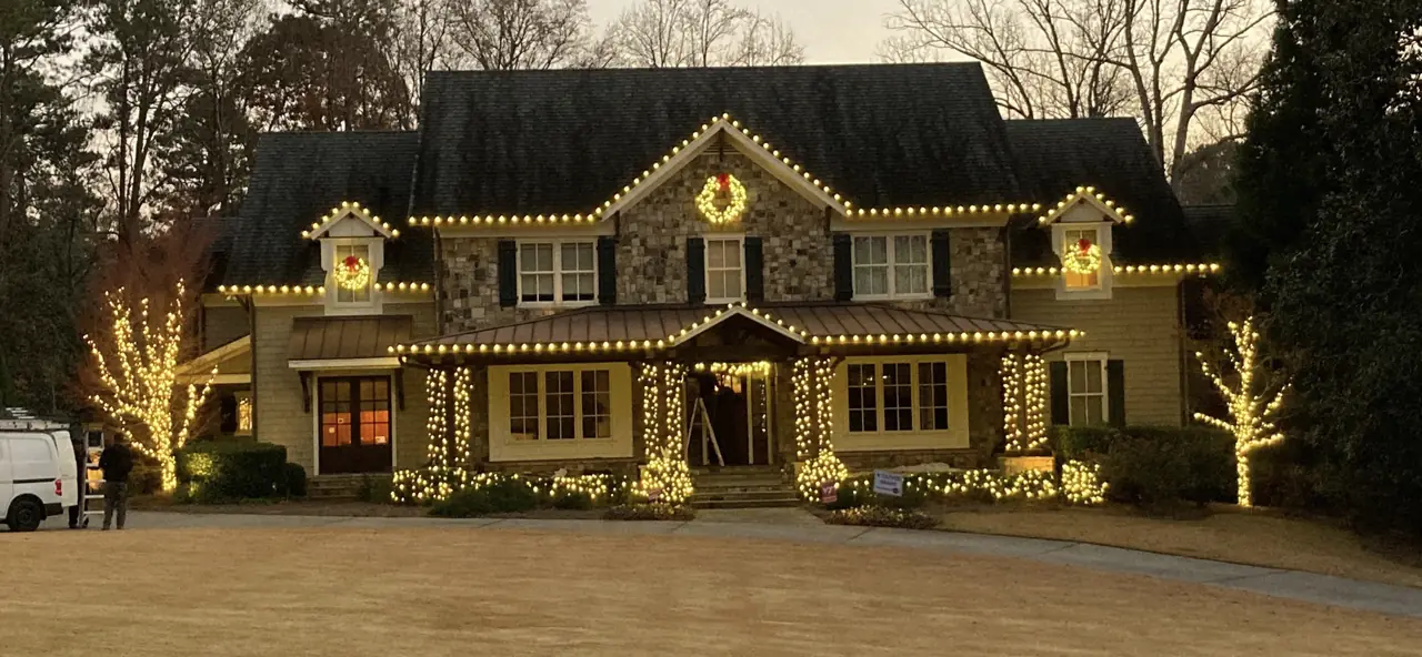 A home decorated with illuminated wreaths, porch garland and warm white roofline lights.